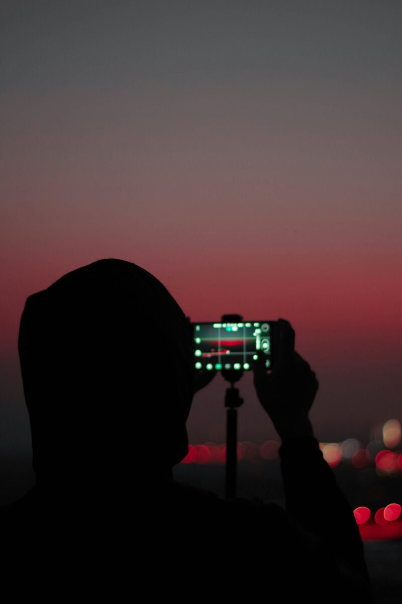 Silhouette d'une personne photographiant le crépuscule avec un téléphone sur trépied.