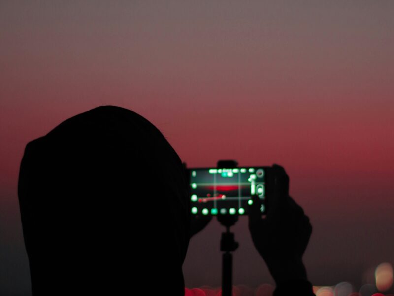Silhouette d'une personne photographiant le crépuscule avec un téléphone sur trépied.