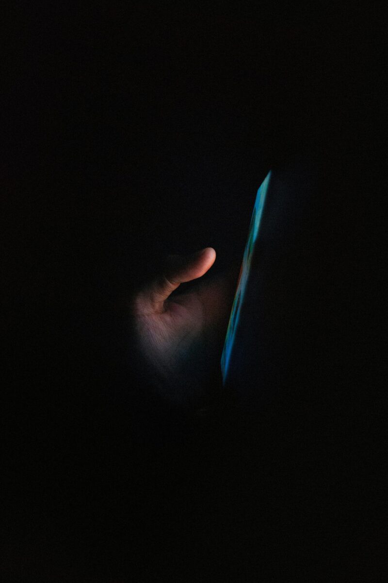 Main tenant un téléphone cellulaire dont l'écran brille dans l'obscurité totale