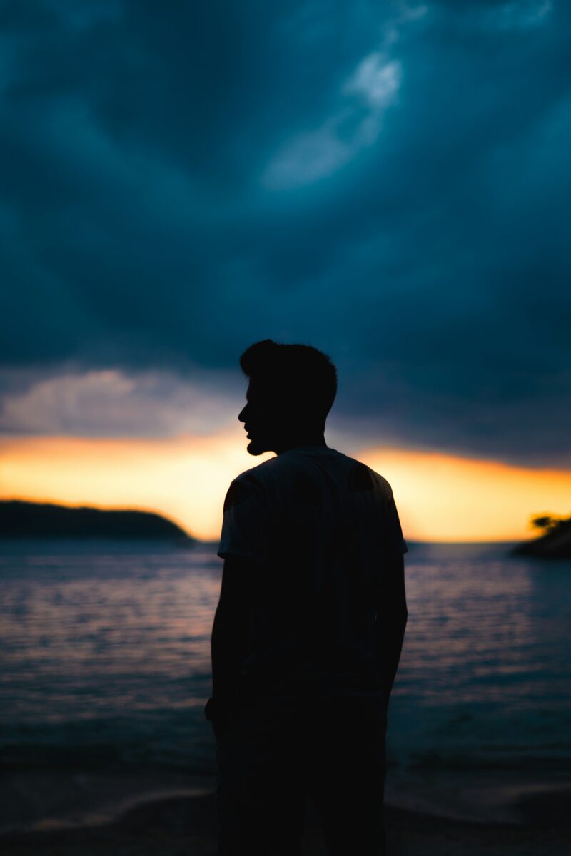 Silhouette sombre d'un homme se détachant sur un ciel coloré au coucher du soleil.