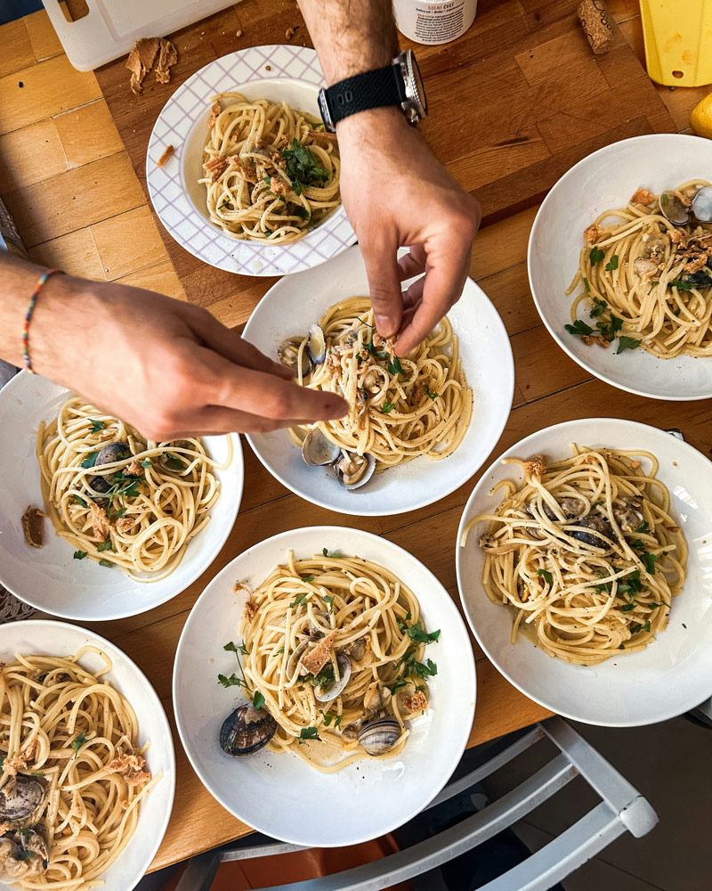 Vue de dessus d'une table en bois où des amis partagent plusieurs assiettes de spaghettis aux palourdes.